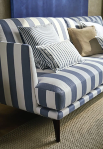 Gestreiftes Polstermöbel in Blau-Weiß mit Dekokissen vor Vorhang