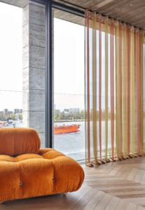 Transparente Wellenvorhänge mit Ausblick auf einen Fluss und orangefarbenem Designersessel